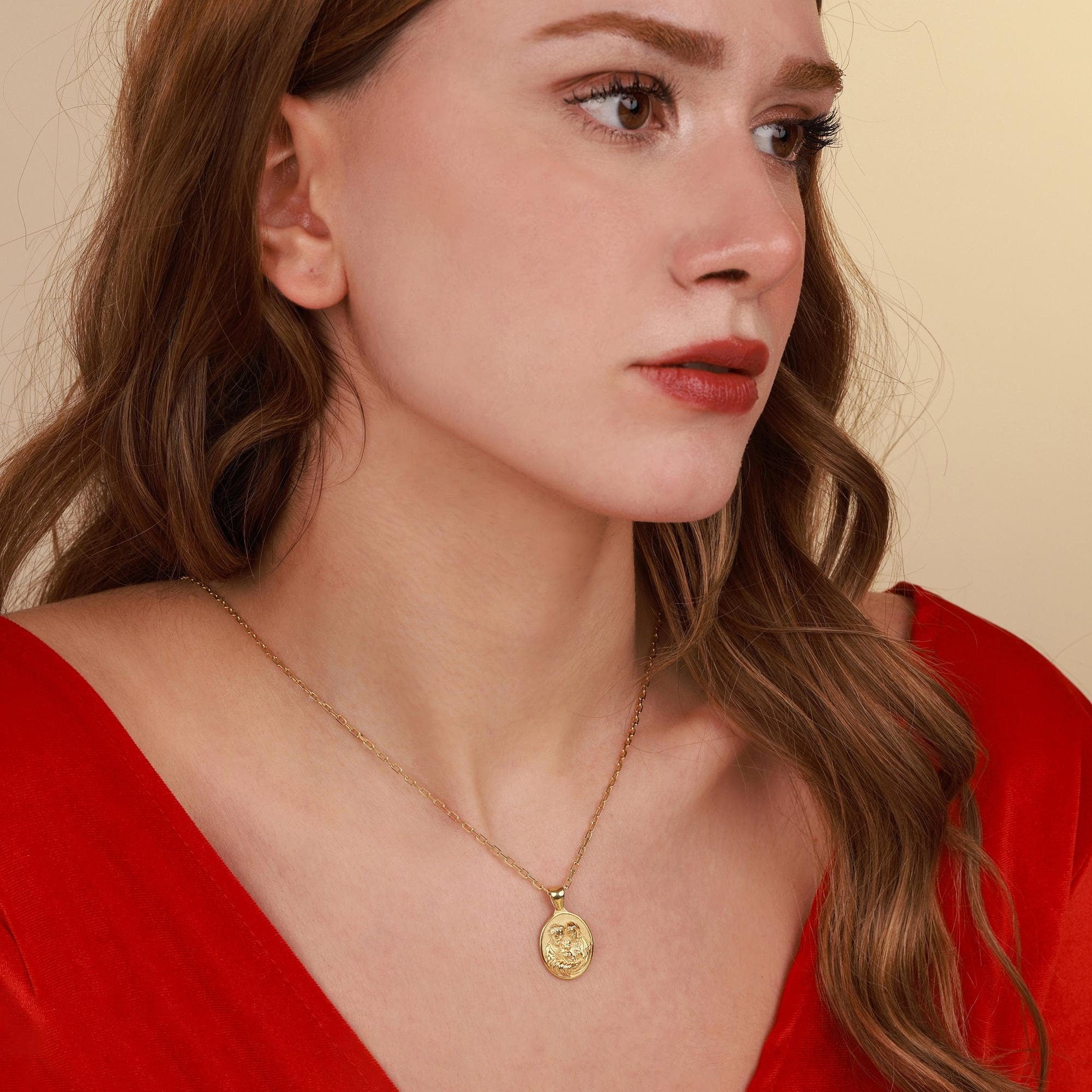 Woman wearing a gold christian necklace with a pendant against a beige background