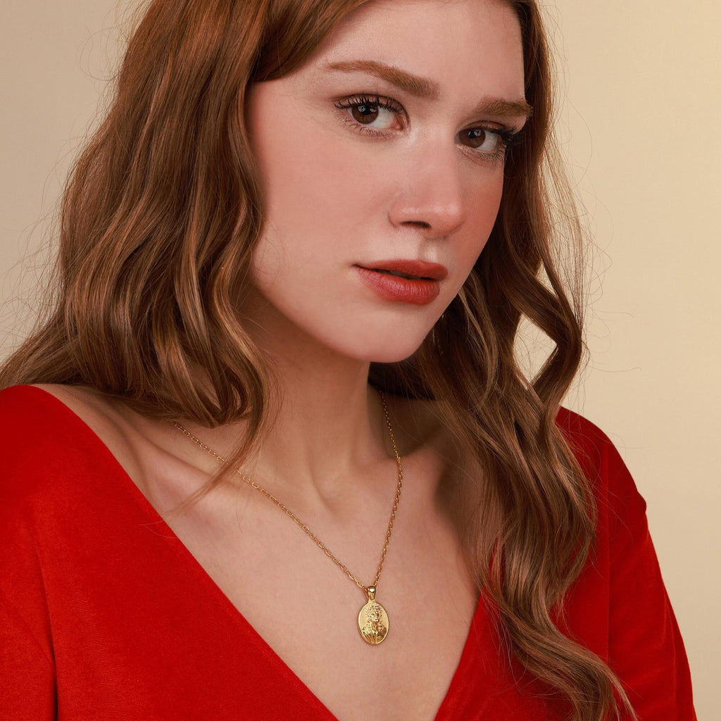 Woman wearing a gold faith necklace with a pendant against a beige background