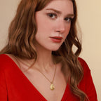 Woman wearing a gold faith necklace with a pendant against a beige background