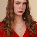 A woman wearing a red top and a gold catholic necklace with a beige background