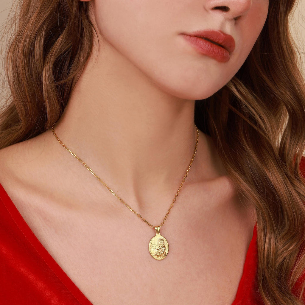 Close-up of a woman wearing a gold necklace with a jesus pendant, against a neutral background.