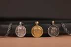 Three Virgin Mary coin pendants on chains against a black and brown gradient background