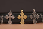 Three cross-shaped pendants in polished silver, gold, and oxidized silver color on a dark background.