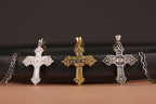 Three Quis ut Deus cross-shaped pendants on a black surface with a brown background