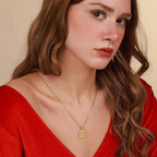Woman wearing a gold birth of jesus necklace with a pendant against a beige background