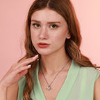 Woman wearing a green top and an oxidized origami bat necklace with a pink background