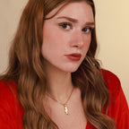 Woman wearing a red top and gold seahorse necklace against a beige background