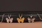 Butterfly-shaped polished silver, oxidized silver, and gold vermeil pendants on chains against a dark background