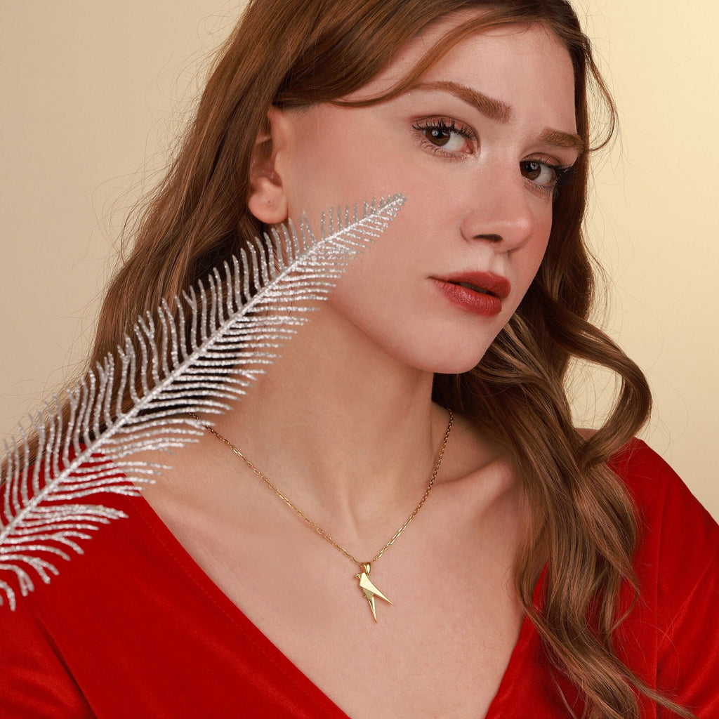 Woman wearing a gold parrot necklace with a feather accessory on a beige background