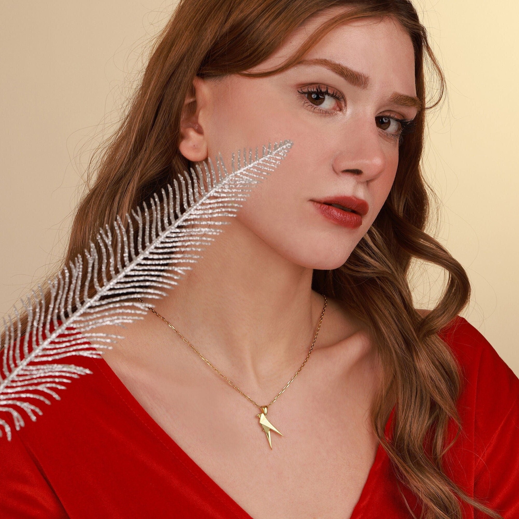 Woman wearing a gold parrot necklace with a feather accessory on a beige background