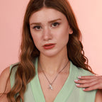 Woman wearing a green top and a sterling silver bird necklace against a pink background