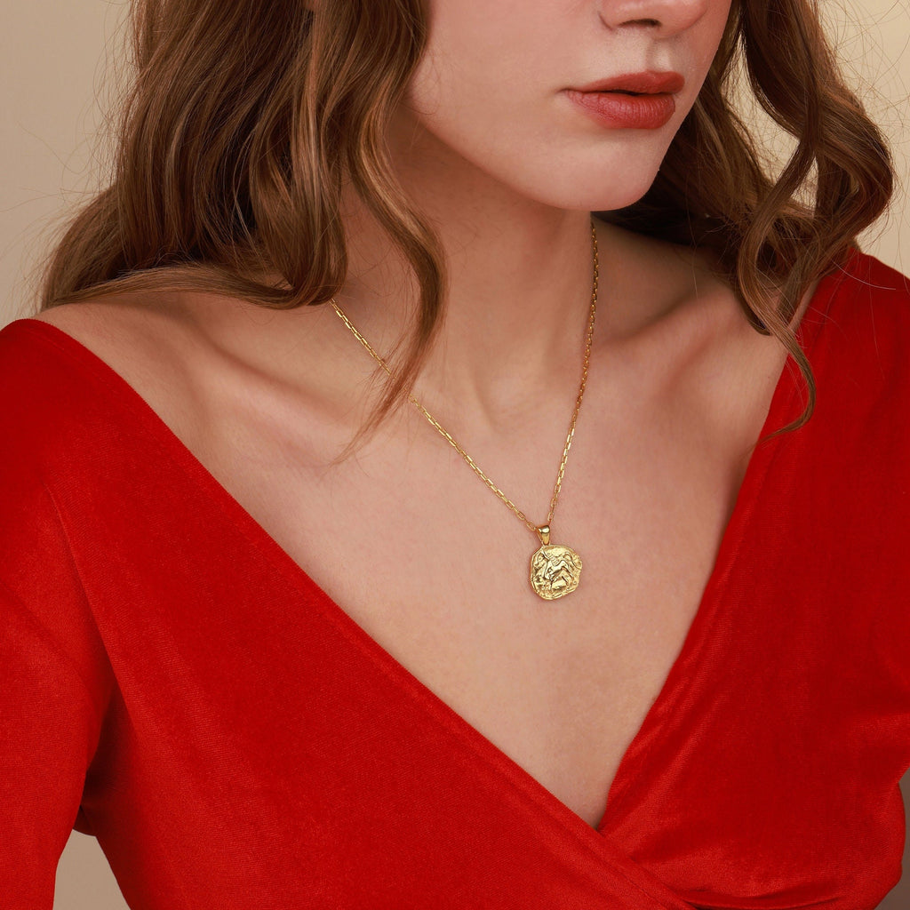 Woman wearing a gold necklace with a red top against a beige background
