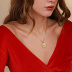 Woman wearing a gold necklace with a red top against a beige background