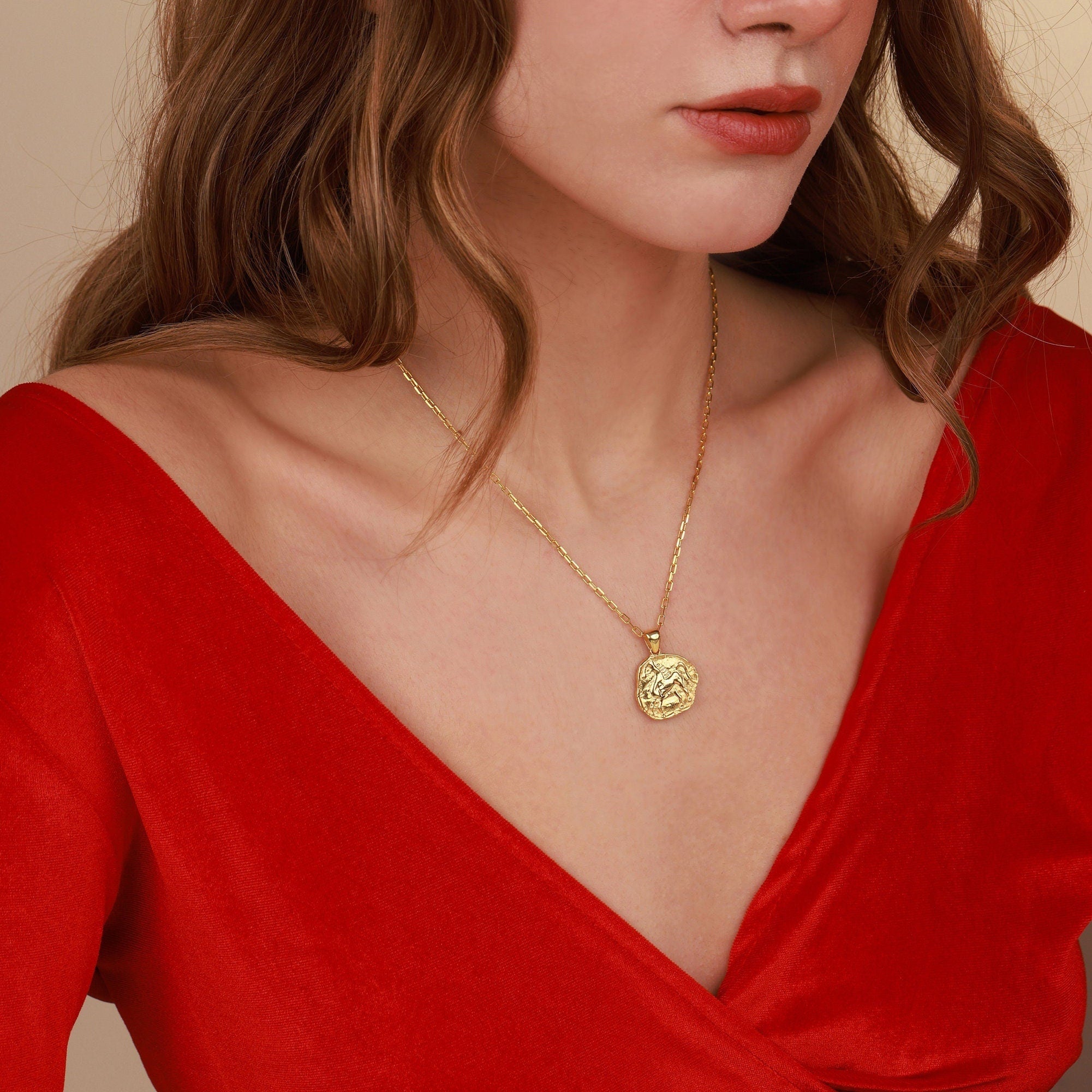 Woman wearing a gold necklace with a red top against a beige background