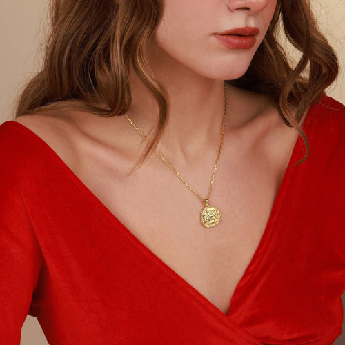 Woman wearing a gold necklace with a red top against a beige background