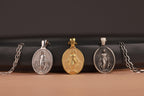 Three miraculous medal pendants on chains against a dark background