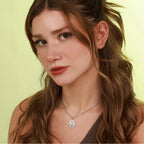 Close-up of a woman with long brown hair and a silver mother mary necklace against a light green background