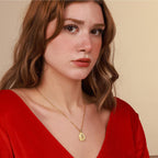 Woman wearing a gold christian necklace with a pendant against a beige background
