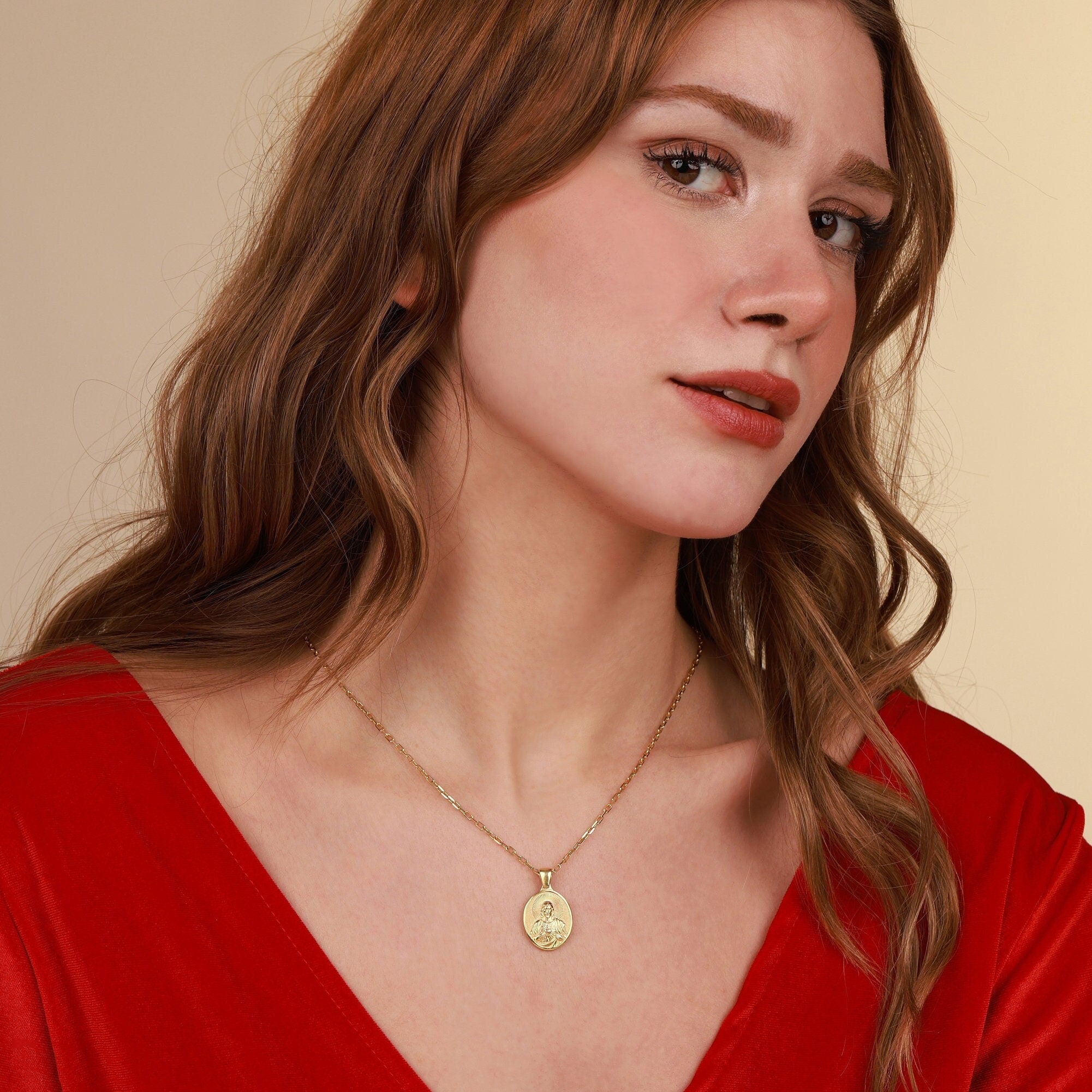 Woman wearing a gold jesus necklace with a pendant against a beige background