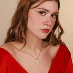 Woman wearing a red top and gold jesus necklace against a beige background