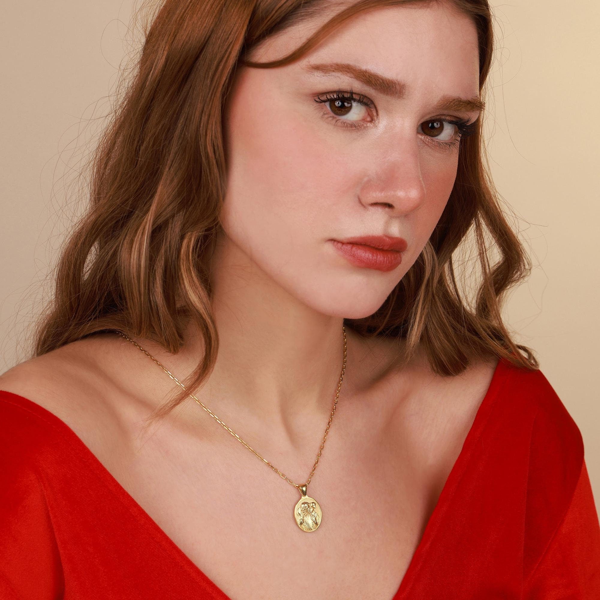 Woman wearing a red top and gold jesus necklace against a beige background