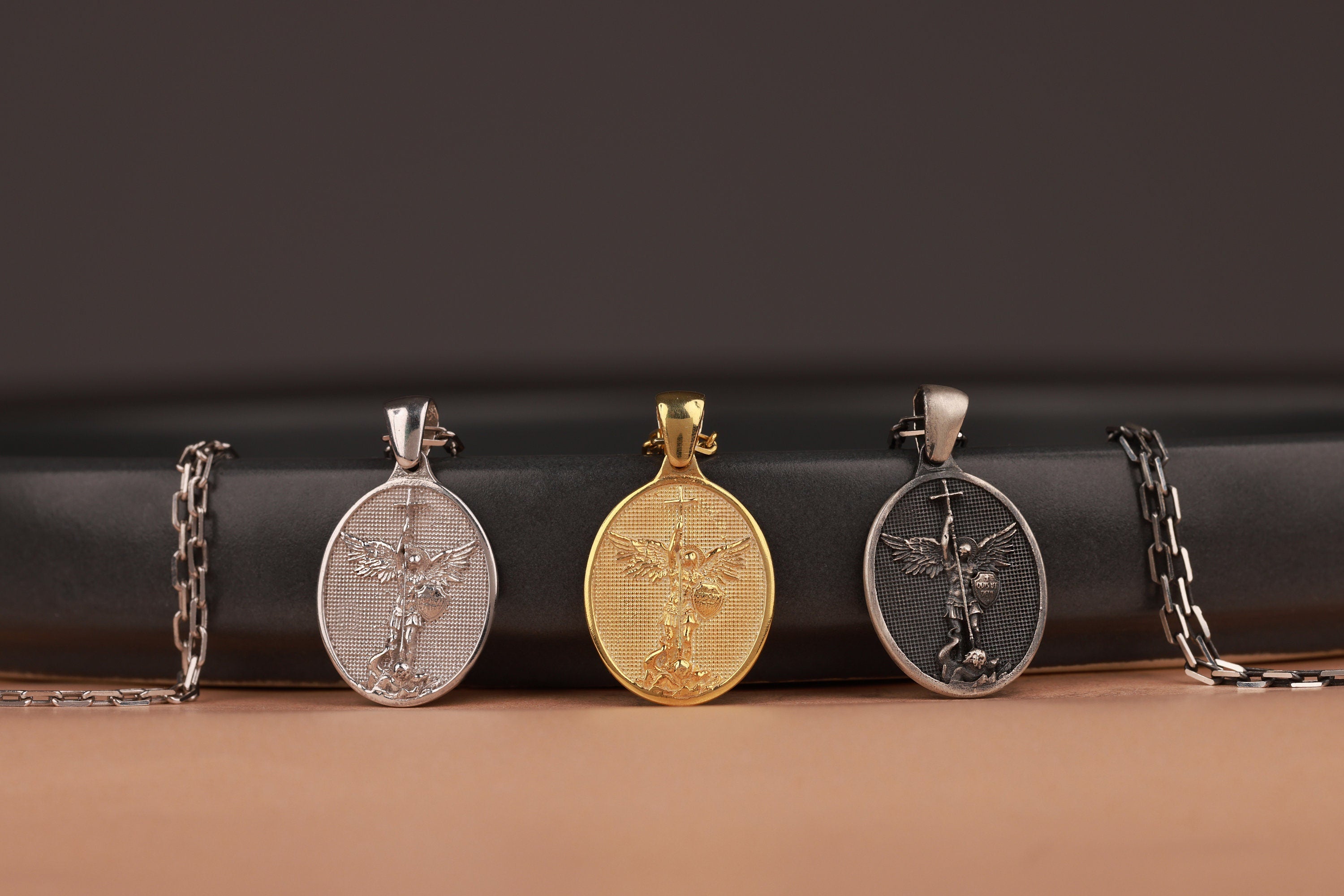 Three St Michael the Archangel pendants on a black and brown gradient background