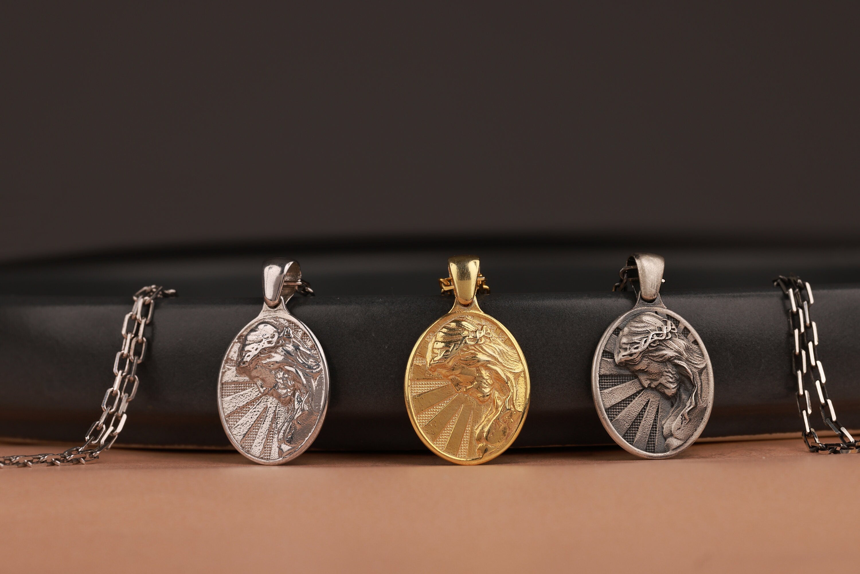 Three oval Jesus pendants on a black and brown gradient background