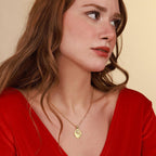 A woman wearing a gold Jesus Christ 
necklace with a pendant against a beige background
