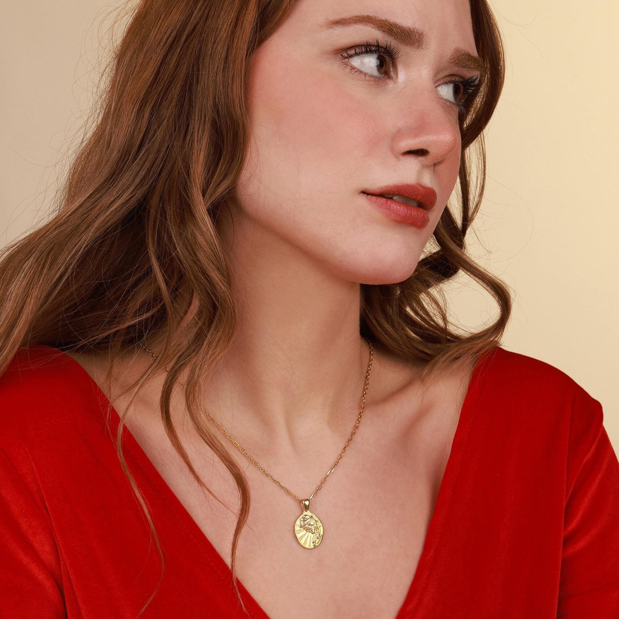 A woman wearing a gold Jesus Christ 
necklace with a pendant against a beige background