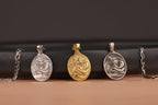 Three oval-shaped Mother Mary pendants on a black cylindrical object with a brown background