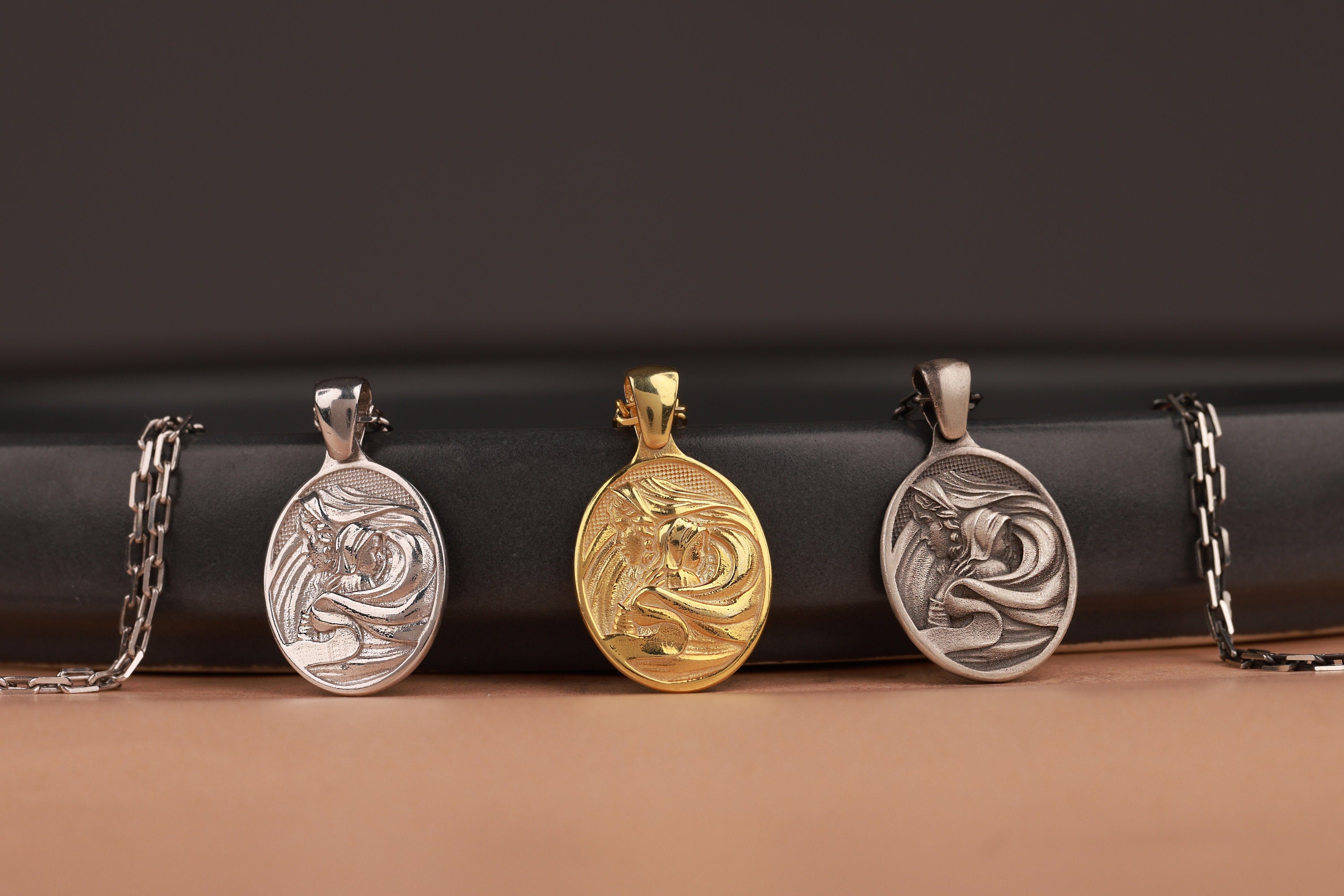 Three oval-shaped Mother Mary pendants on a black cylindrical object with a brown background