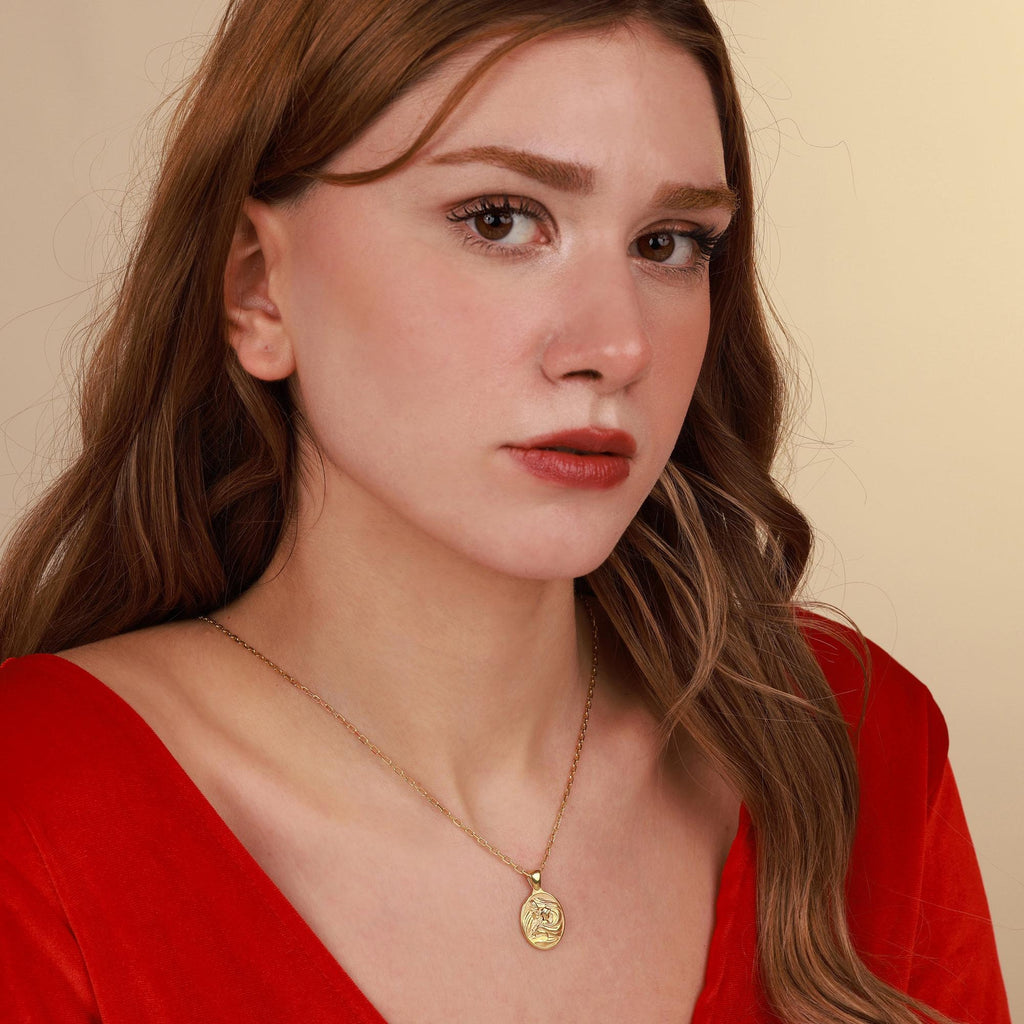 Woman wearing a red top and gold necklace with a virgin mary pendant against a beige background