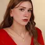Woman wearing a red top and gold necklace with a virgin mary pendant against a beige background