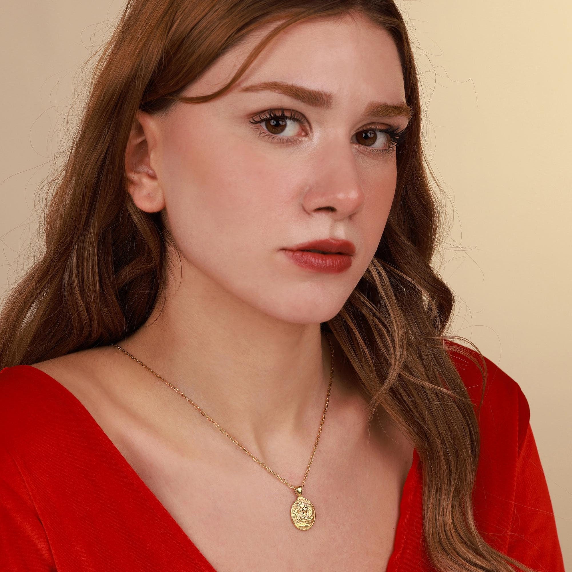Woman wearing a red top and gold necklace with a virgin mary pendant against a beige background