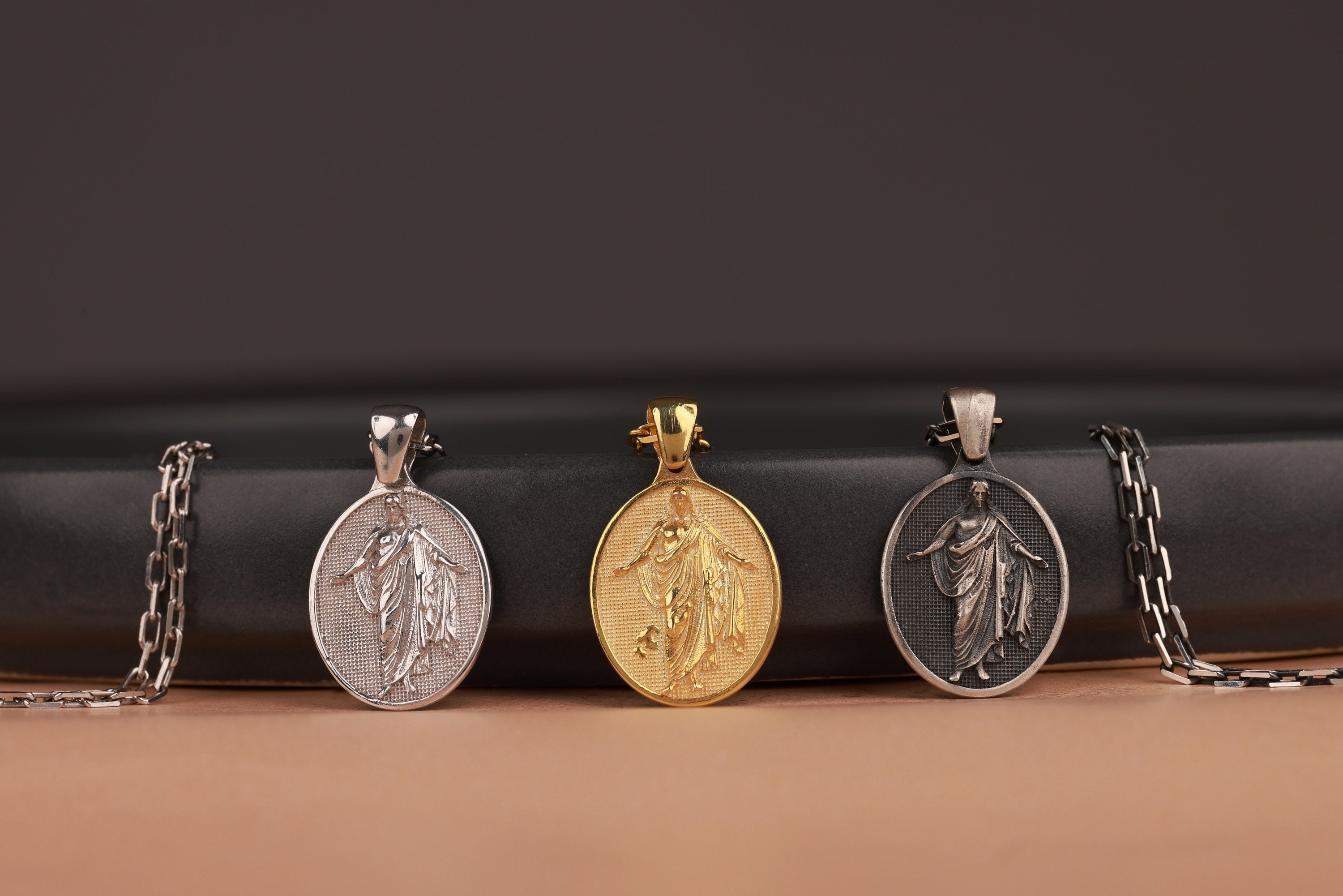 Three risen Jesus pendants on chains against a dark background