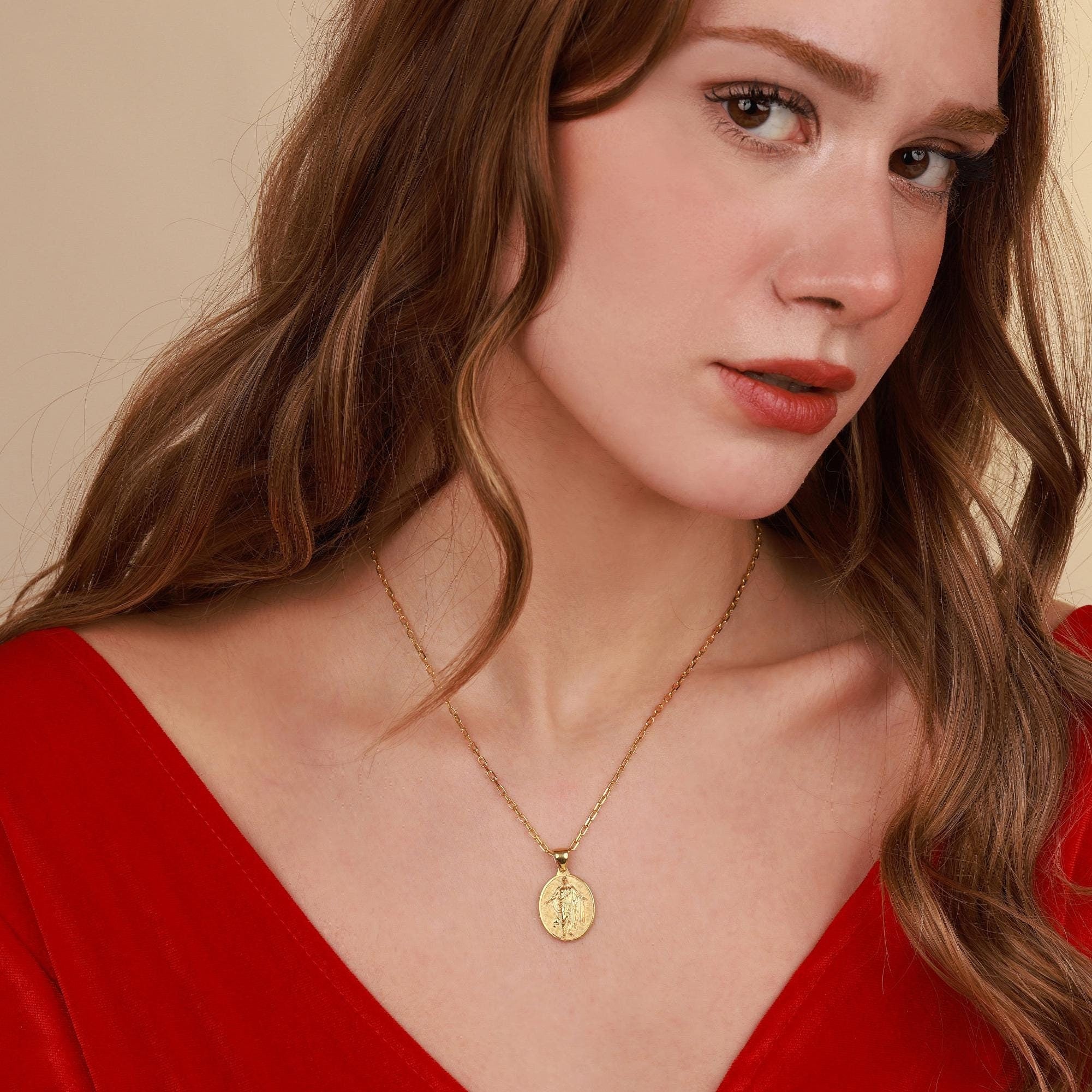 Woman wearing a gold Risen Savior necklace with a pendant against a beige background