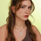 Woman wearing a polished silver necklace with a jesus cross pendant against a light green background