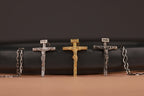 Three crucifixion of Jesus Catholic pendant of different finishes on a brown surface with a black background
