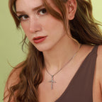 Woman wearing a polished sterling silver necklace with a cross pendant against a green background