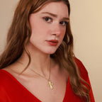 Woman wearing a gold vermeil necklace with an ornate cross pendant against a beige background