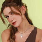 Woman wearing a polished sterling silver necklace with an ornate cross pendant against a light green background