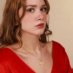 Woman wearing a gold necklace with a crucifix pendant against a beige background