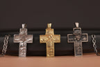 Three detailed cross pendants on a dark surface with a brown background