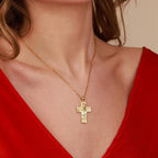 A gold cross necklace featuring the crucifixion of Jesus on a person wearing a red top against a neutral background