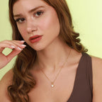 Woman wearing a gold necklace with a heart pendant against a light green background
