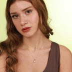 Woman wearing a necklace with a heart pendant against a light green background