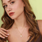 Woman wearing a gold necklace with an opal pendant against a light green background