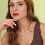 Woman wearing a necklace with an opal pendant against a light green background