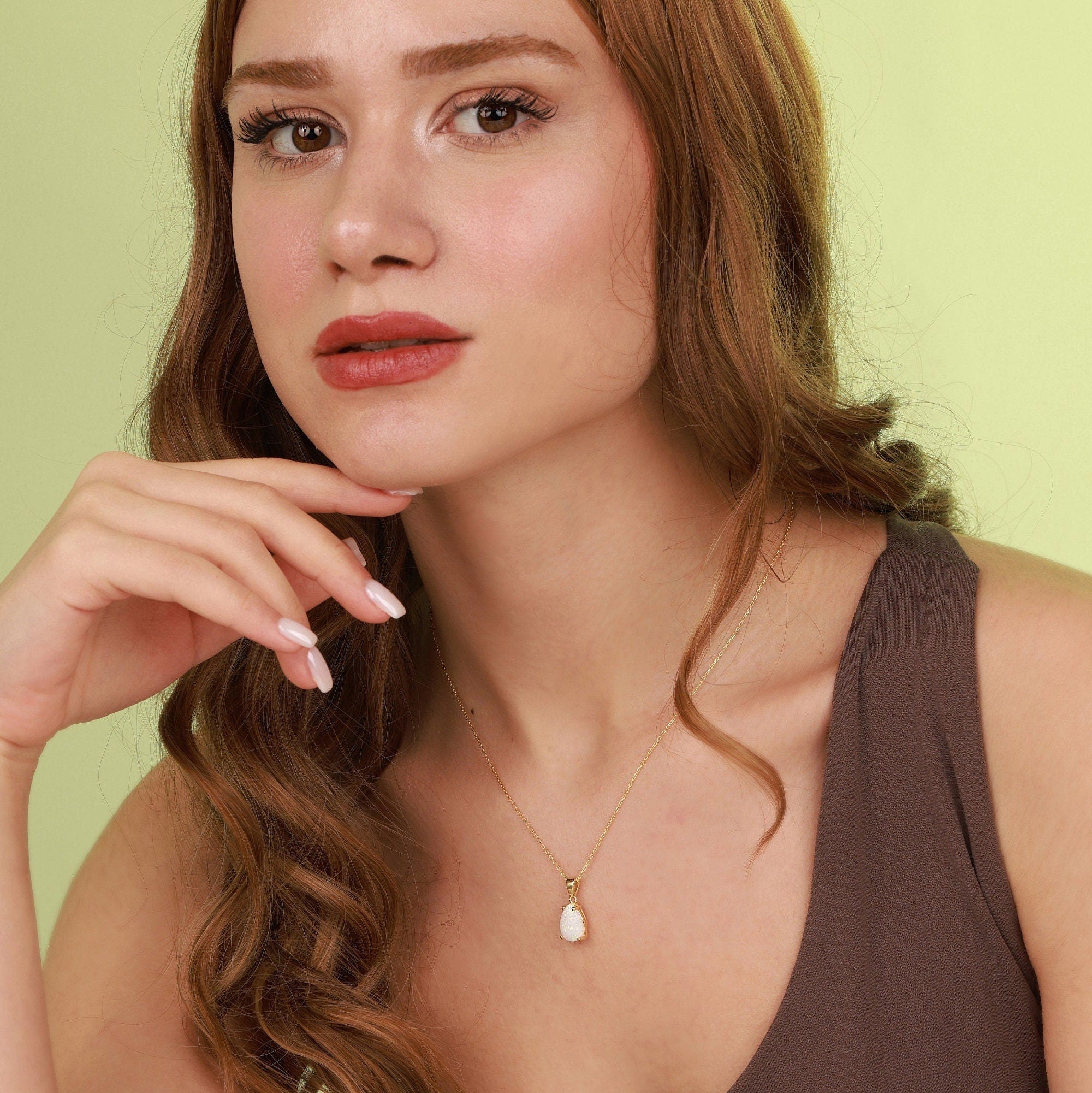 Woman wearing a necklace with an opal pendant against a light green background