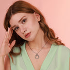 Woman wearing a green top and silver necklace against a pink background